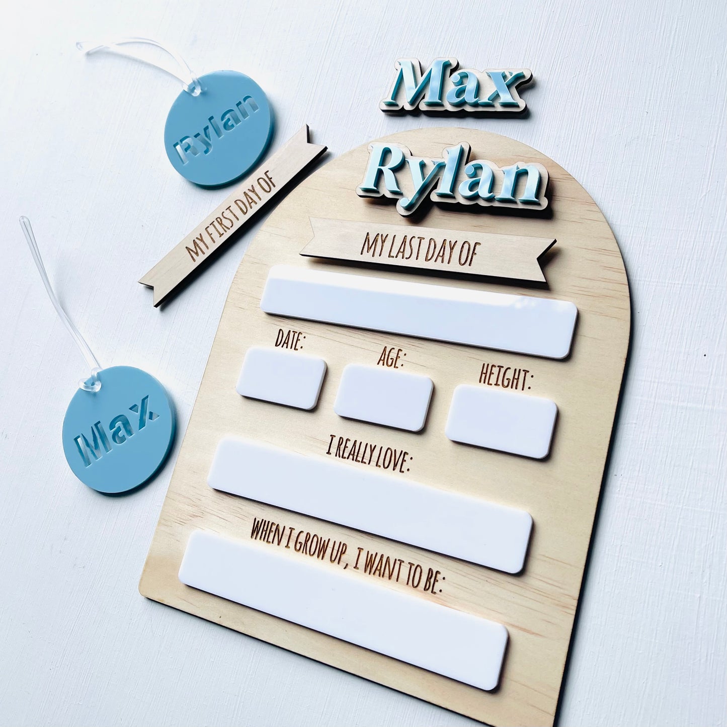 Wooden board with name tags and questionnaires for 'My First Day of Kindergarten' and 'My Last Day of Kindergarten' on a white background.