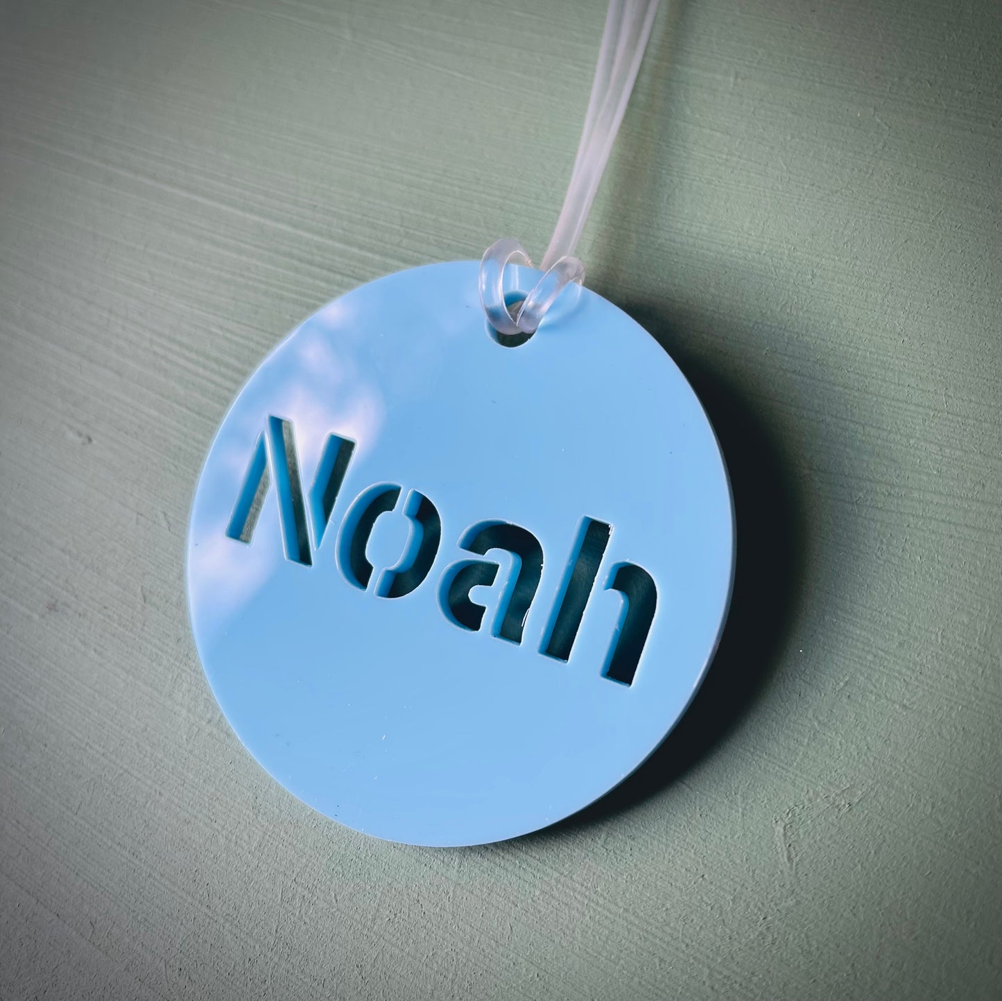 Round blue tag with 'Noah' engraved on a light green background