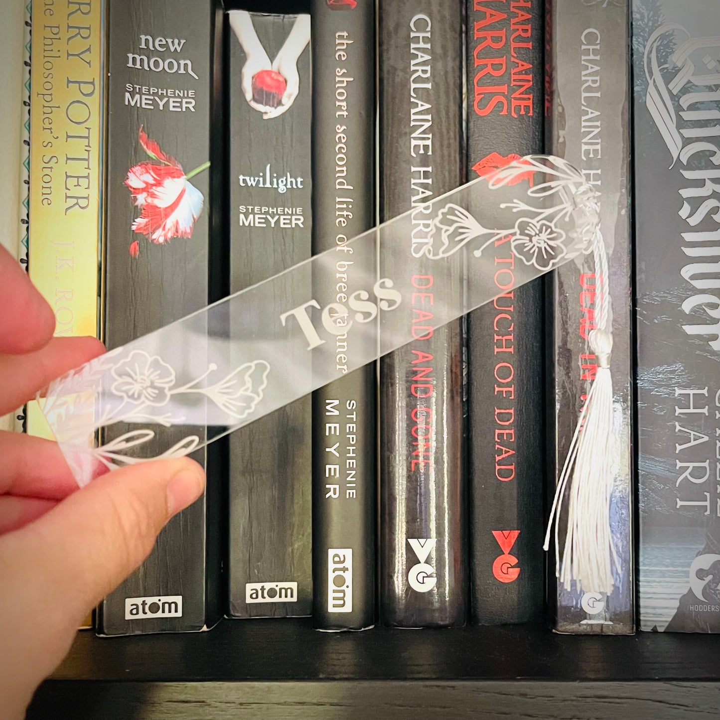 Hand holding a clear bookmark with floral design in front of a row of books.