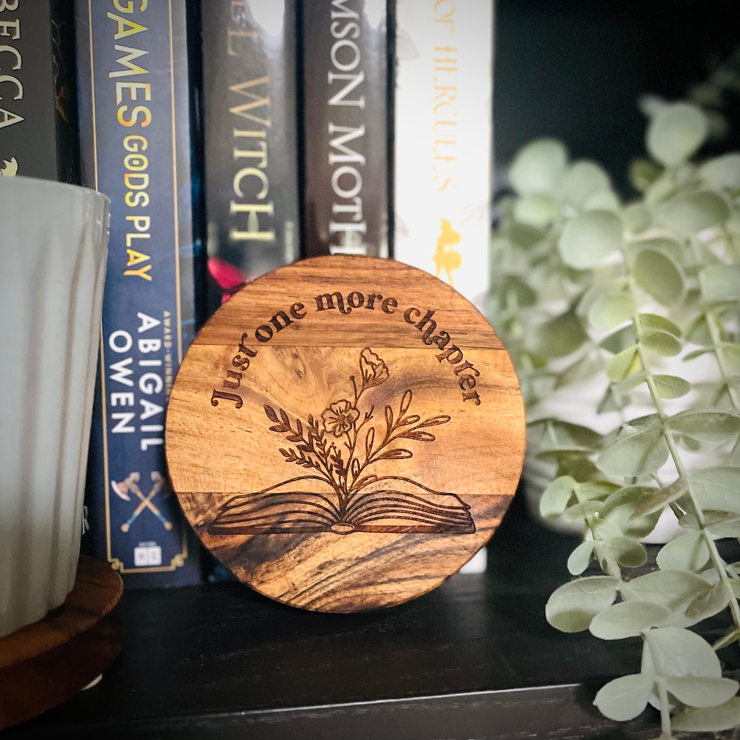 Wooden coaster with 'Just one more chapter' text and floral design on a bookshelf background.