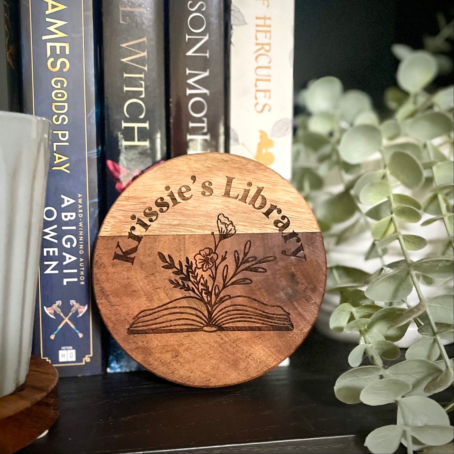 Wooden disc with  Library engraving in front of books on a shelf.