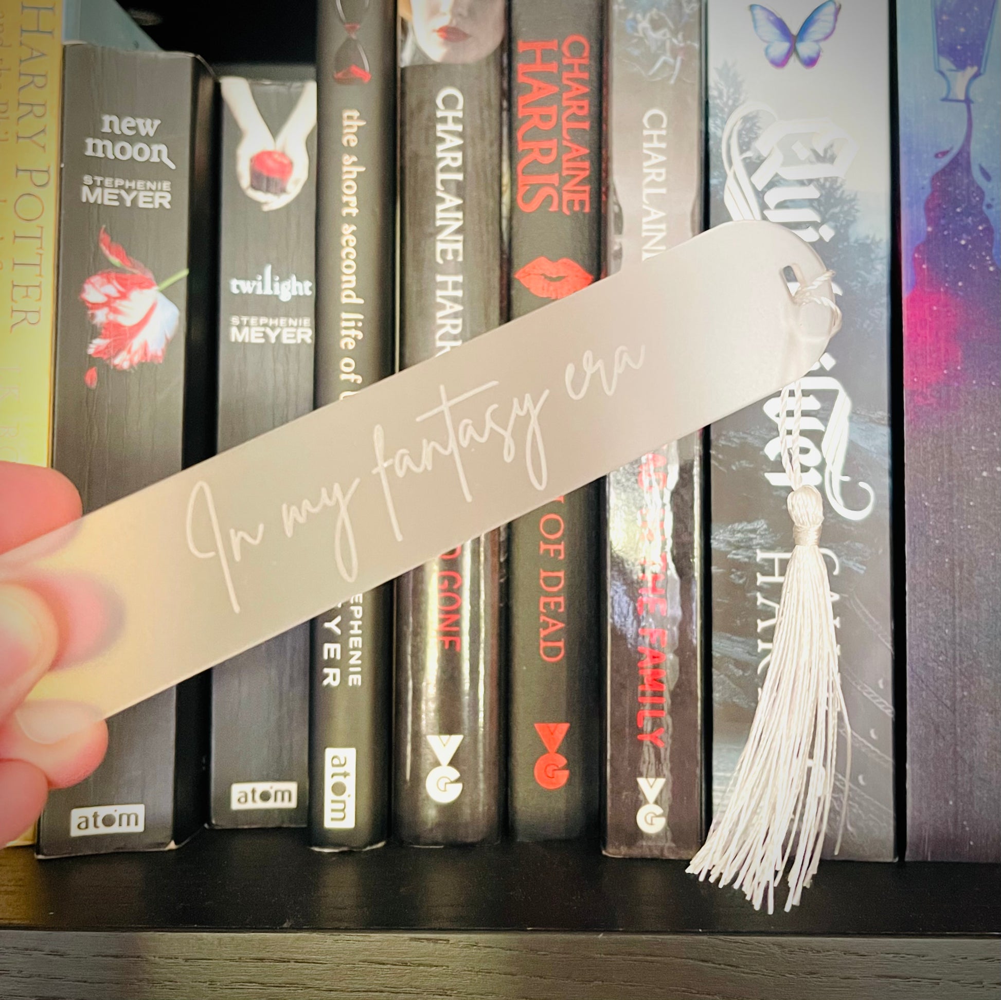 Bookmark with tassel held in front of books on a shelf